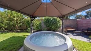 Un bain à remous installé sous une terrasse couverte, avec un mur en briques et des meubles d’extérieur.