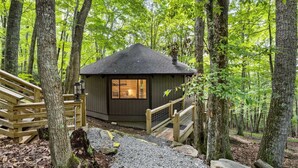 Une petite cabane à toit sombre, entourée de grands arbres et dotée d’une terrasse en bois.