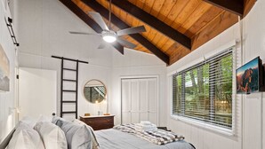 Une chambre à coucher comprenant un lit, une commode, un miroir, un ventilateur de plafond et une fenêtre avec des stores.