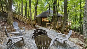Une cabane entourée d’arbres, dotée d’une terrasse en gravier, d’une plateforme en bois et de fauteuils Adirondack.