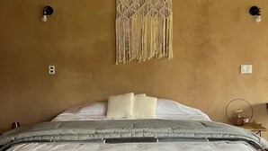 Un lit avec un cadre en bois, une literie blanche et une décoration murale en macramé.