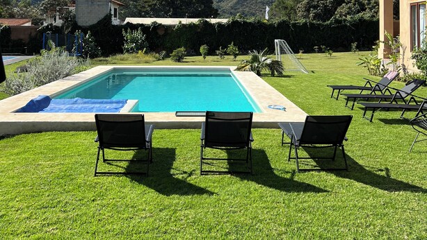 Une piscine entourée de chaises longues, avec une pelouse bien entretenue et une chaîne de montagnes en toile de fond.