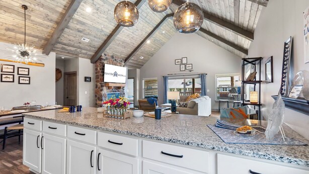A spacious kitchen with a granite countertop, white cabinets, and a stone accent wall. There are hanging pendant lights and a large window providing natural light. - New Log Cabin with Ozark Views, Free Daily Local Attraction Tickets & Community Amenities (Branson)