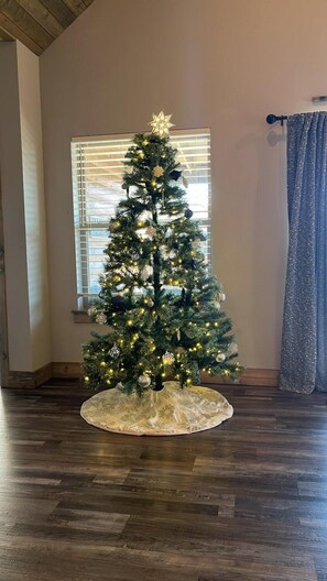 Un árbol de Navidad en una habitación con piso de madera y una ventana con persianas.