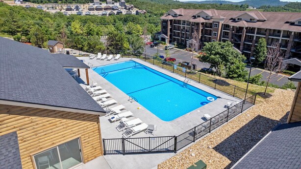 Un hotel con piscina, sillones de descanso y vistas al bosque y edificios circundantes.