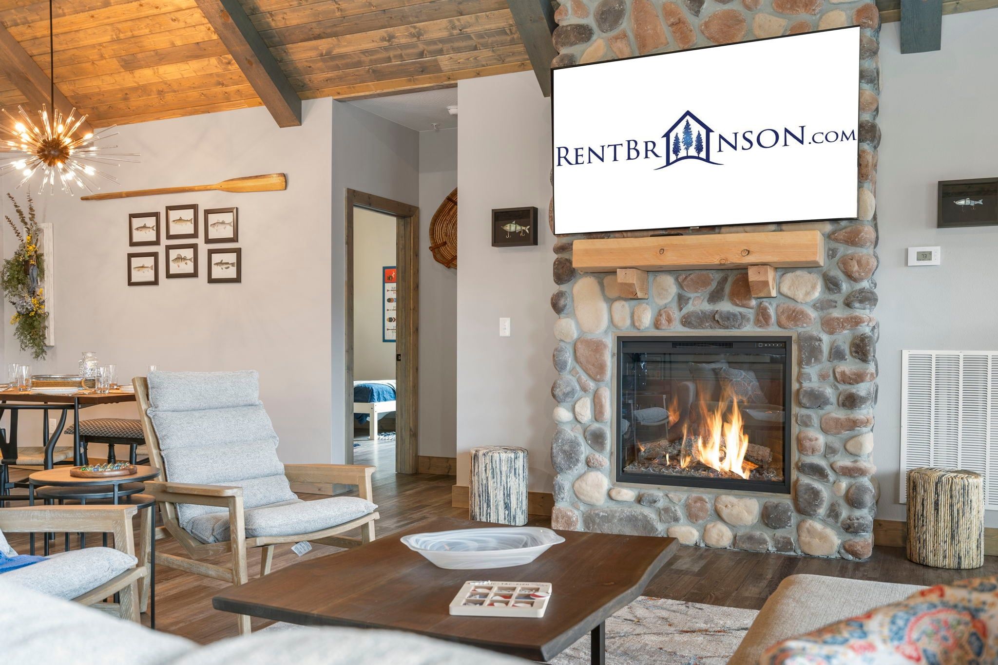 A cozy living room with a stone fireplace, wooden furniture, and a dining area with a table set for four.