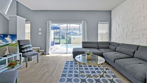 A modern living room with a grey sofa, a glass coffee table, and a TV on a stand. - Encantada Resort: Pool, Gym, Clubhouse, 10min to Disney (Kissimmee)