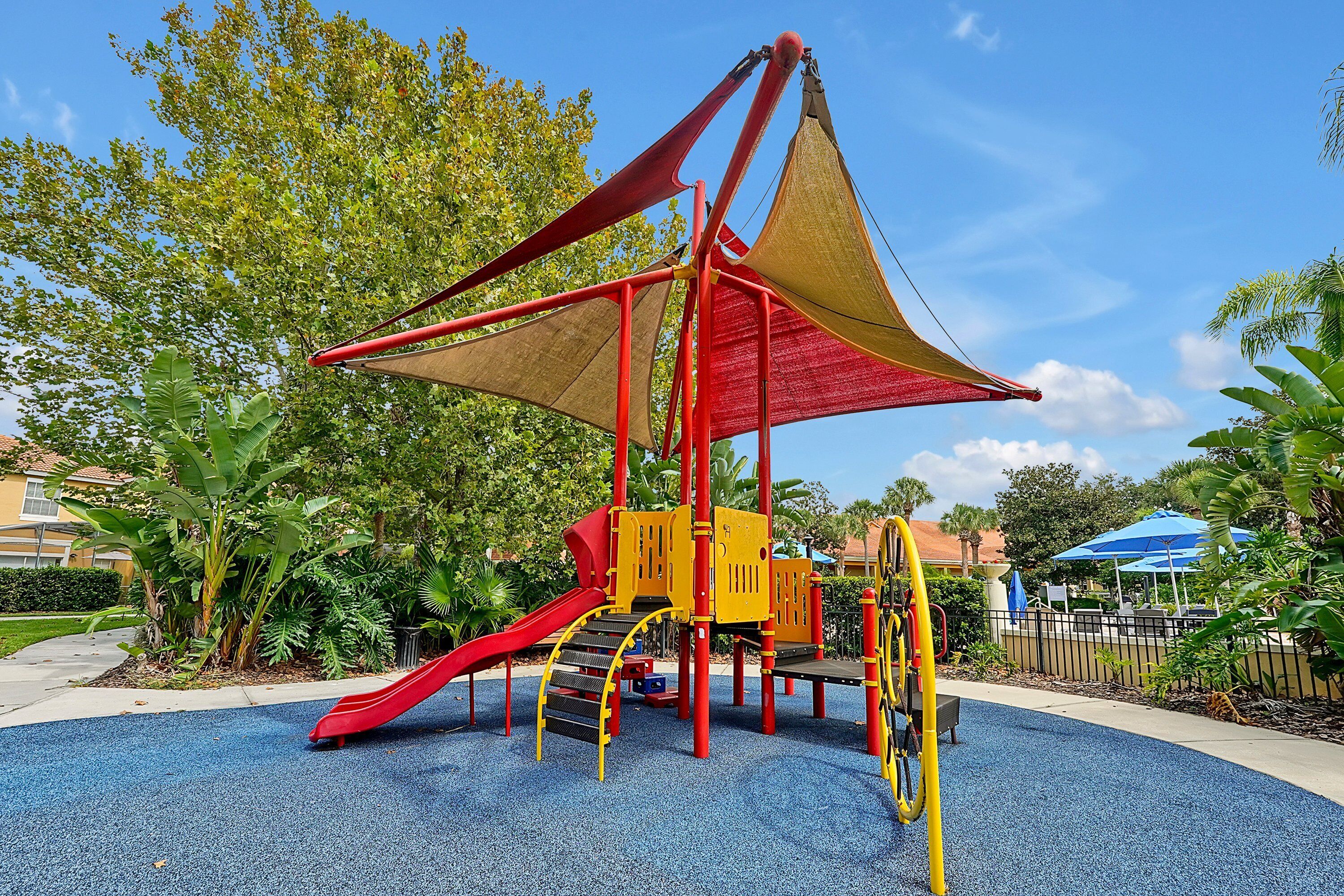 A playground with a red slide, yellow and red play structures, and a blue sky.