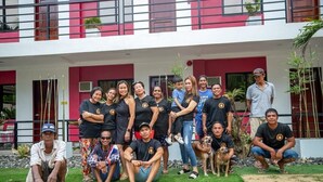A group of people posing in front of a modern building with a red and white facade, a balcony, and some greenery. - Room 805 @ Pennington Inn, Guimaras (Western Visayas)
