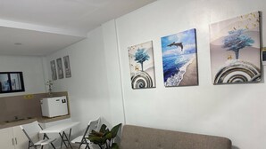 A modern living room with a grey sofa, a dining table with chairs, and a small kitchen area with a refrigerator. There are three wall-mounted paintings depicting nature scenes. - Room 805 @ Pennington Inn, Guimaras (Western Visayas)