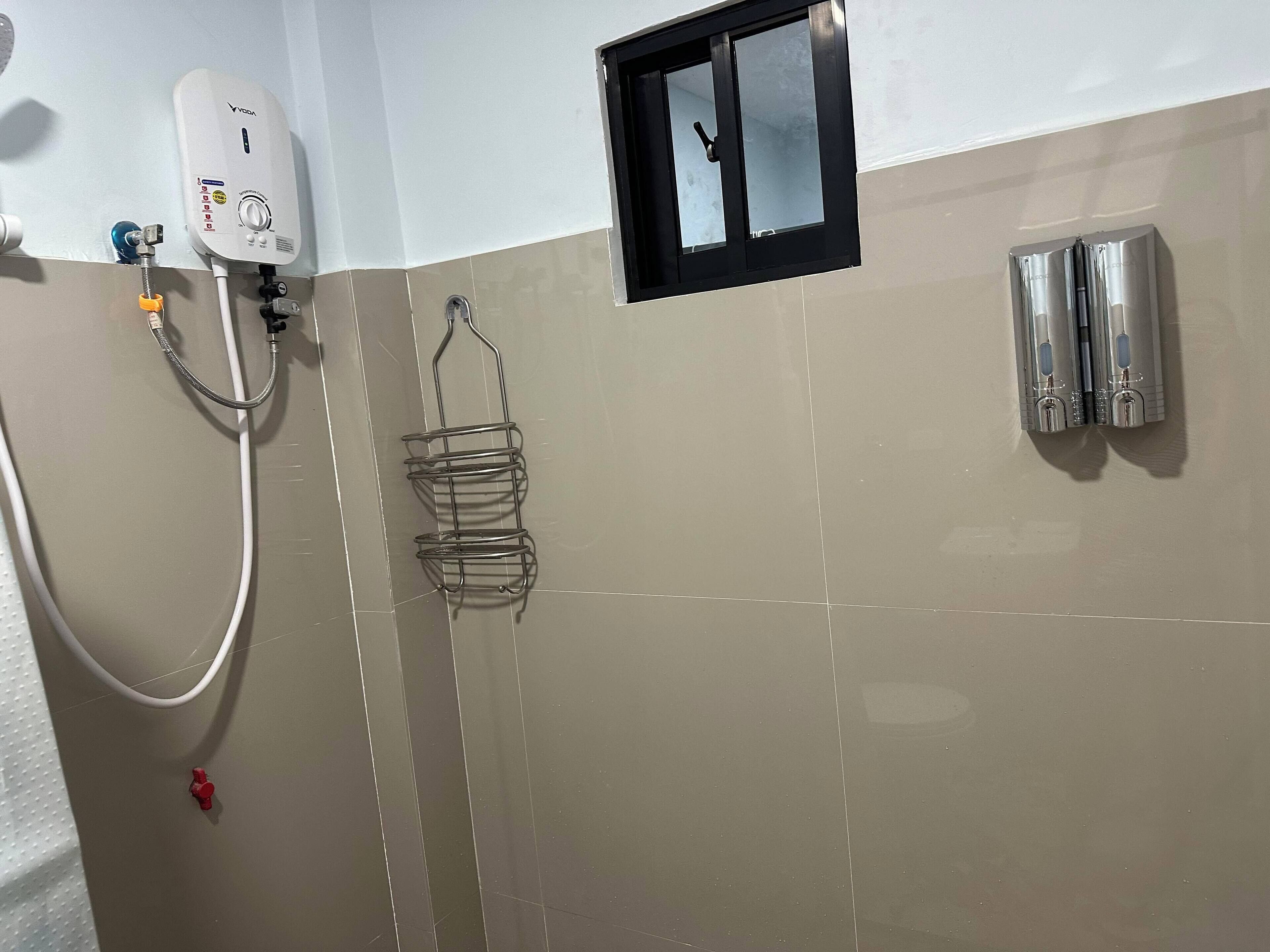 A bathroom with a white and beige tiled wall, a handheld showerhead, a metal rack, and two wall-mounted faucets.