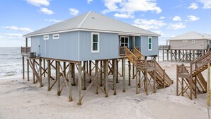 A beach house with a balcony and a staircase leading to the entrance.