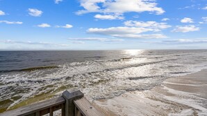 A beach with waves, a wooden boardwalk, and a clear sky.