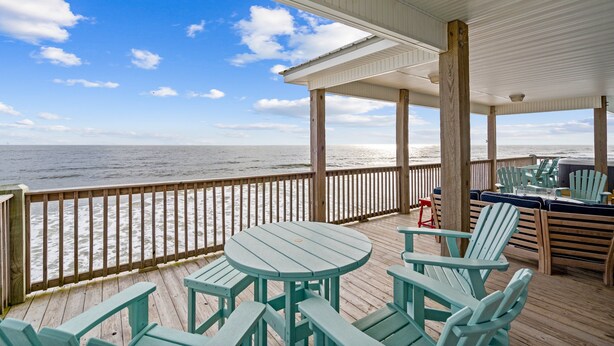 A covered outdoor deck with wooden furniture and a view of the ocean.