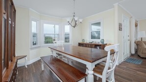 A dining room with a wooden table and white chairs, large windows, and a chandelier. - 4770 - I'm Free - Semi-Oceanfront Oasis w/ Pool & Hot Tub (Kitty Hawk)
