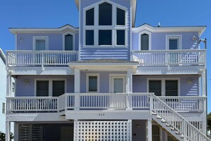 A multi-story building with a balcony on each floor, a central entrance with a door, and a staircase leading to the upper levels. - 1620 - Triple 7, an 8-bed 5.5-bath Corolla NC, private pool, hot tub, game room (Corolla)