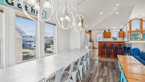 A modern kitchen with a central island, bar stools, and a view of the neighborhood. - 1620 - Triple 7 - Corolla Sleeps 20 | Pool, Hot Tub & Beach Walk (Corolla)