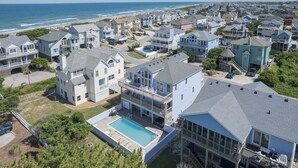 A coastal residential area with houses, a swimming pool, and a view of the ocean. - 1620 - Triple 7 - Corolla Sleeps 20 | Pool, Hot Tub & Beach Walk (Corolla)