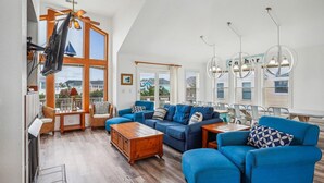 A spacious living room with a high ceiling, large windows, and a view of the outside. - 1620 - Triple 7 - Corolla Sleeps 20 | Pool, Hot Tub & Beach Walk (Corolla)