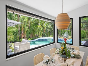 A dining area with a view of a swimming pool and lush greenery. - Modern Tropical Oasis, Private Heated Pool, Minutes to Beach & Wilton Manors! (Wilton Manors)