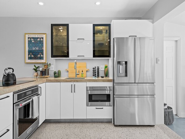 A modern kitchen with stainless steel appliances, white cabinetry, and a granite countertop. - Modern Tropical Oasis, Private Heated Pool, Minutes to Beach & Wilton Manors! (Wilton Manors)
