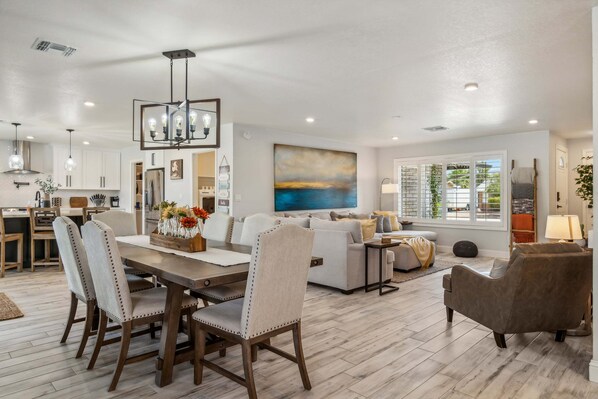 A spacious living area with a dining table, chairs, a sofa, and a large painting.