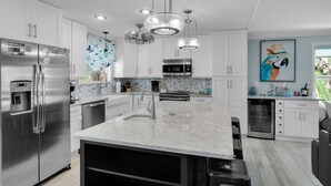 A modern kitchen with stainless steel appliances, white cabinets, a marble island, and pendant lighting. - Rest A Shore Waterfront Home, Brand New Private Pool (Marathon)