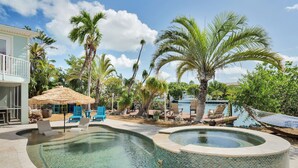 A pool area with lounge chairs, a hot tub, and a thatched-roof structure.