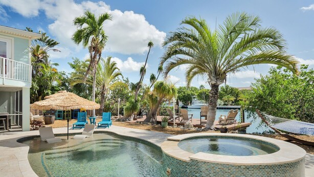 A pool area with lounge chairs, a hot tub, and a thatched-roof structure. - Rest A Shore Waterfront Home, Brand New Private Pool (Marathon)