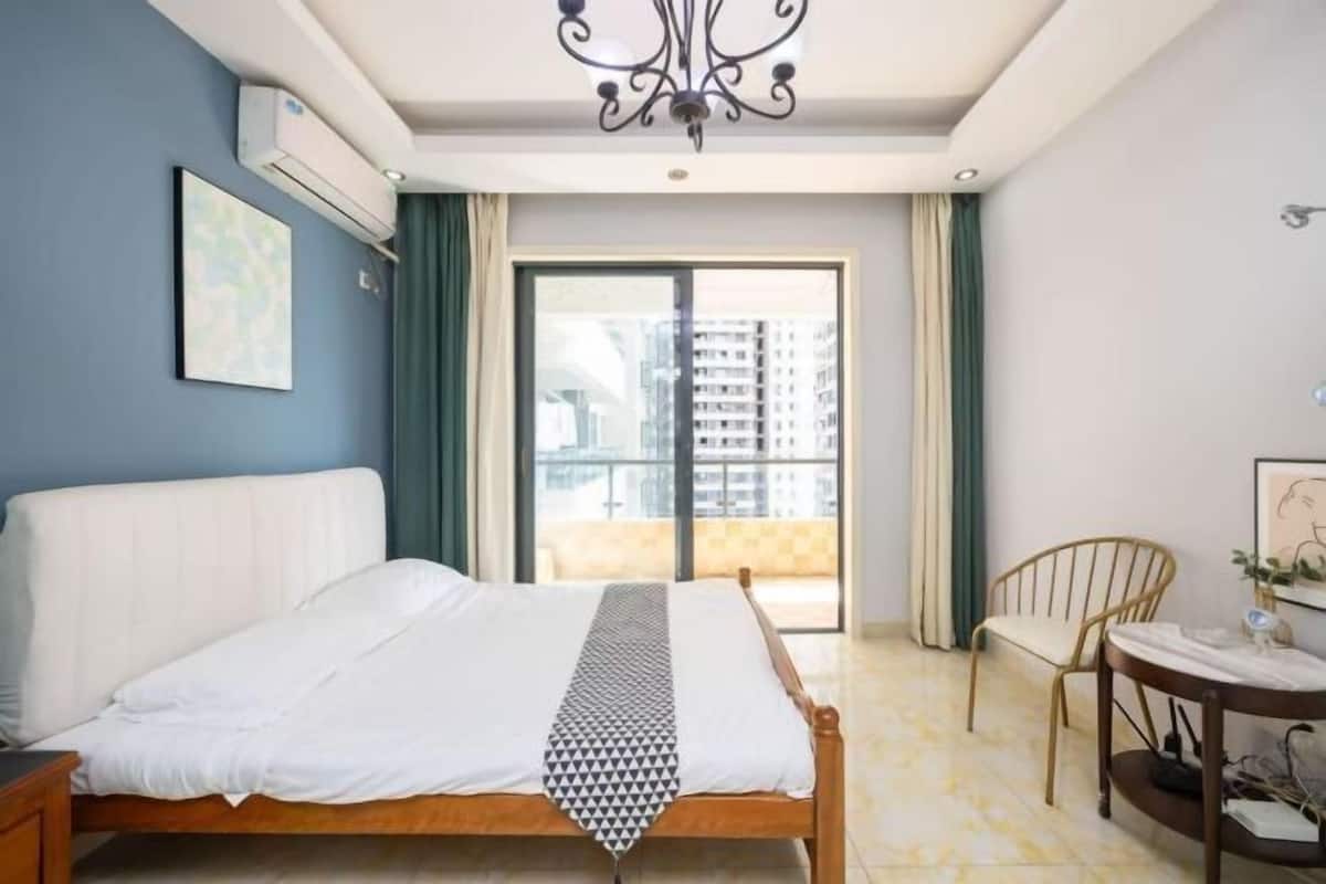 Een slaapkamer met een bed, een stoel, een tafel en uitzicht op gebouwen door een raam.