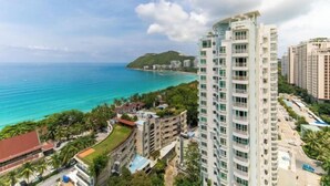 A high-rise hotel with multiple balconies overlooking a coastal area with clear blue waters and a hilly landscape in the background. - Sanya Seaside Breeze Homestay (Sanya)
