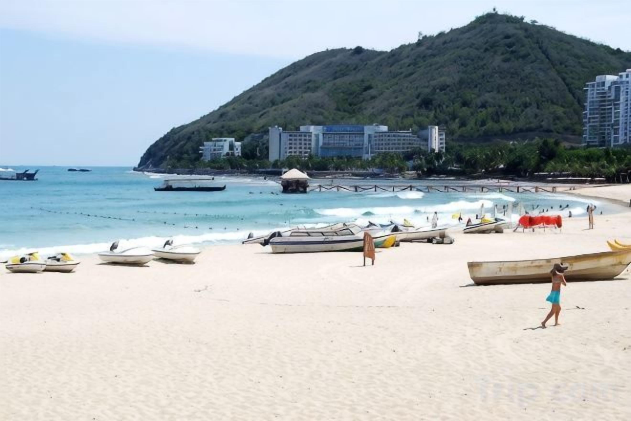 Una playa con barcos, un muelle y edificios al fondo.