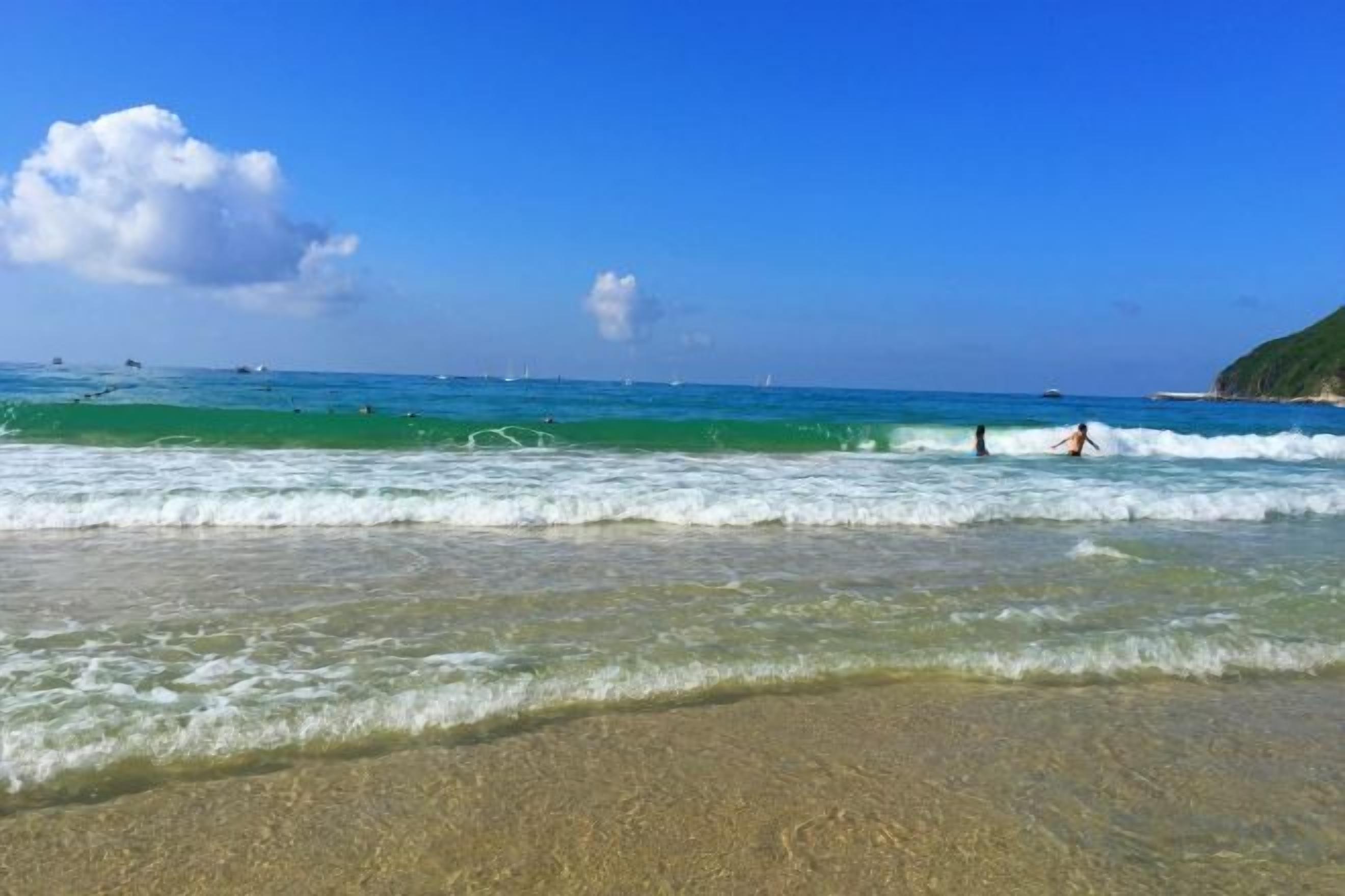 A beach with clear water, a sandy shore, and a distant coastline.