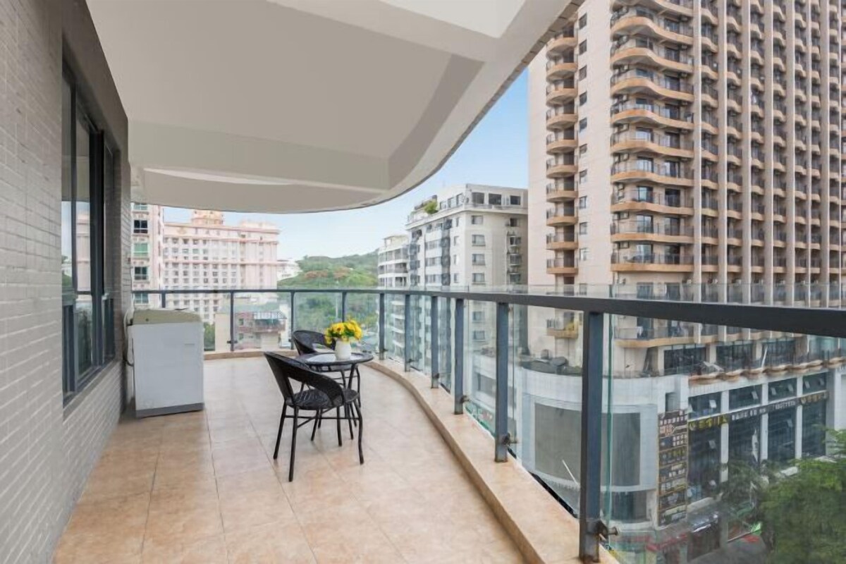 A balcony with a table and chairs, a refrigerator, and a view of surrounding buildings.