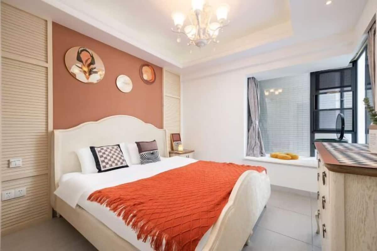 Een slaapkamer met een bed, nachtkastjes, een raam en een kroonluchter.