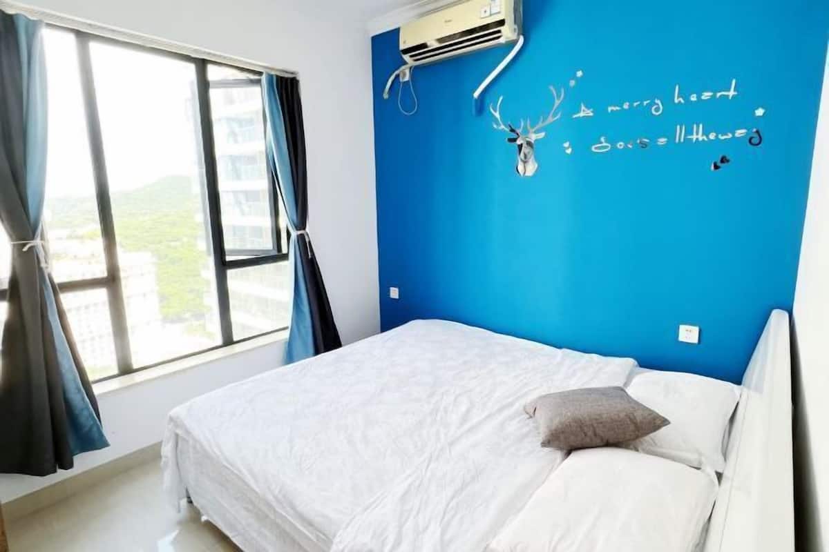 Een slaapkamer met een bed, een raam met gordijnen en een blauwe muur met een hertenkop en tekst.