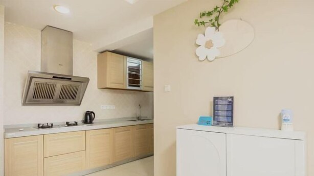 Une cuisine avec des meubles en bois, une hotte de cuisine en acier inoxydable, un réfrigérateur blanc et une décoration florale fixée au mur.