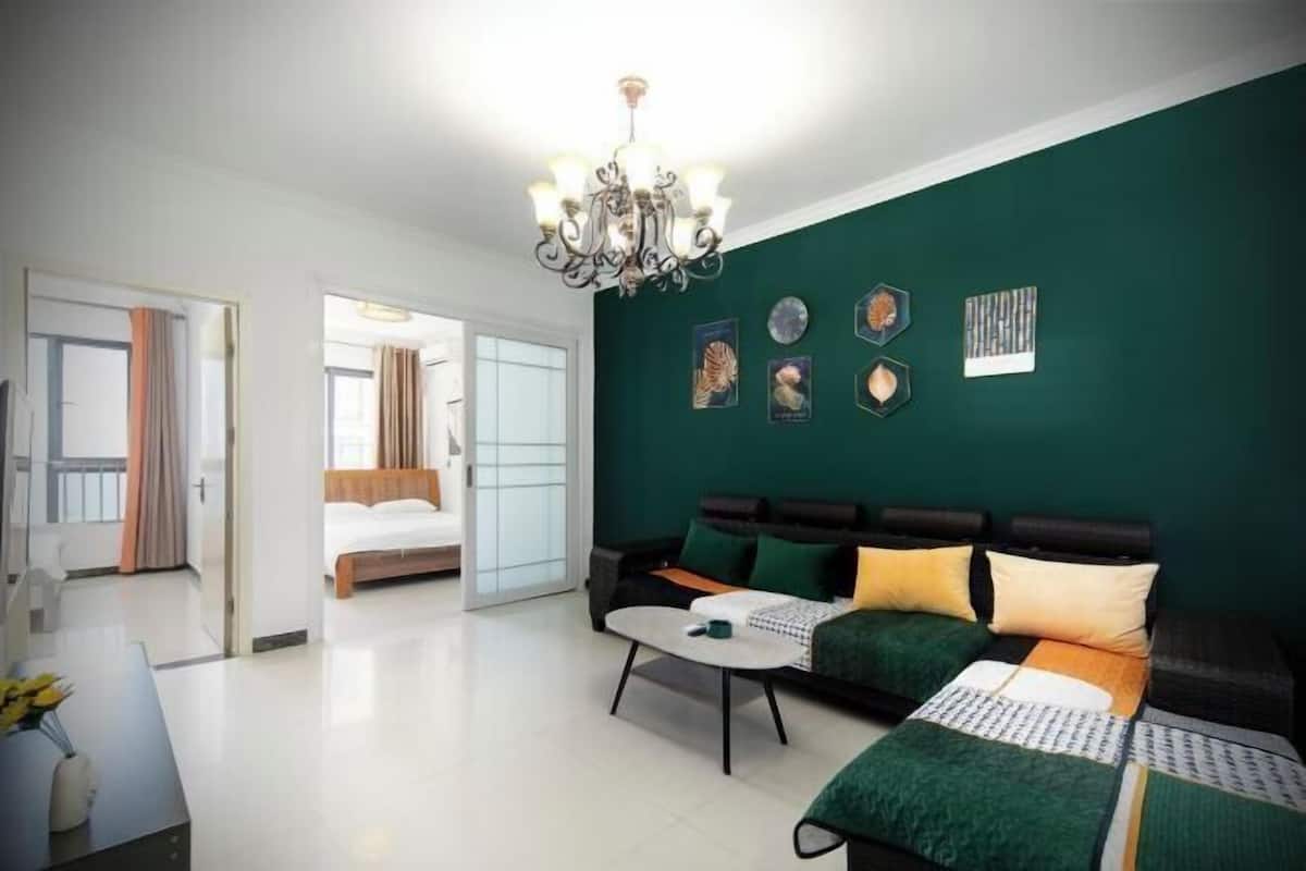 Een moderne hotelkamer met een groene accentmuur, een bank, een bed, een eettafel en een kroonluchter.