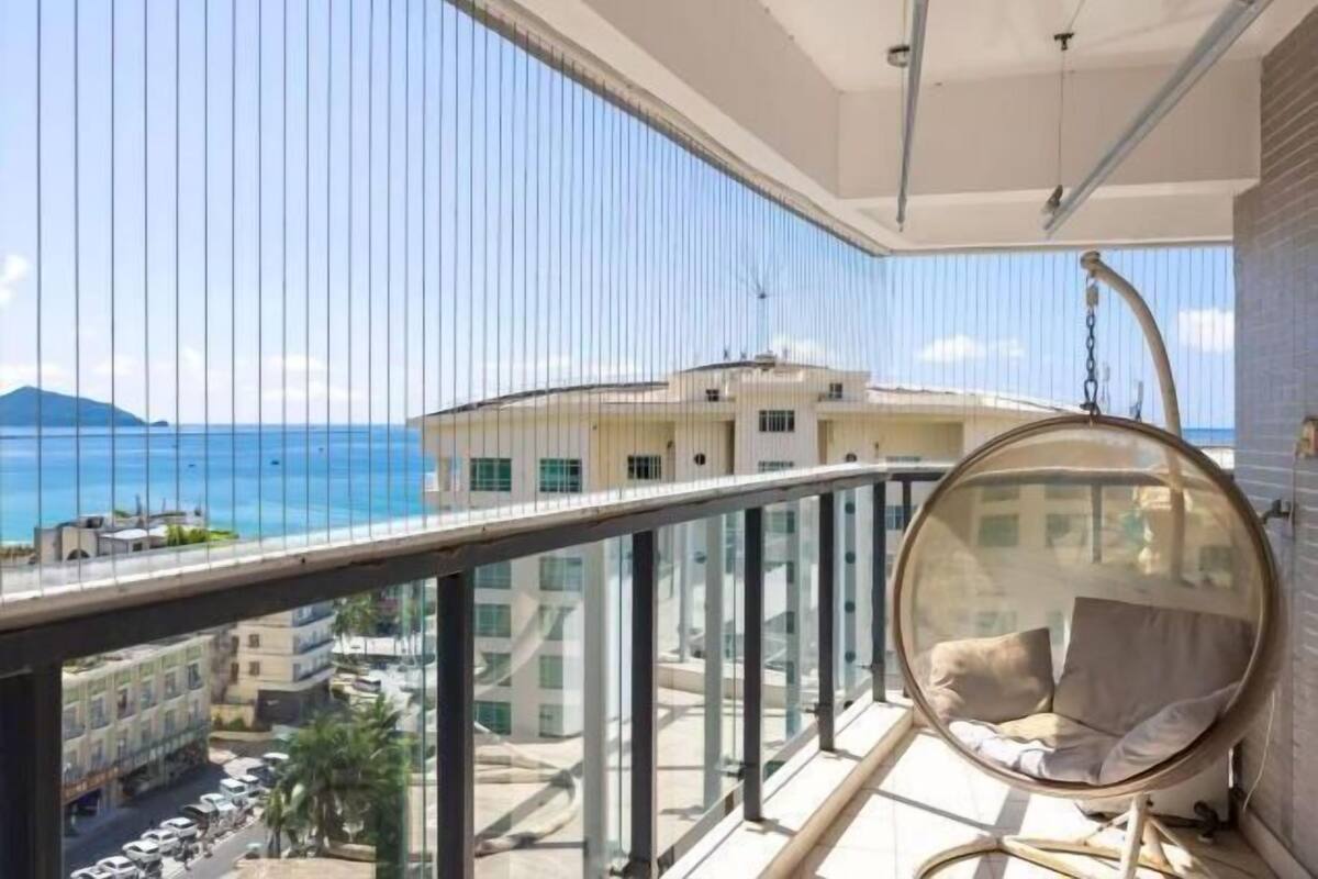 Een balkon met een hangstoel, uitzicht op zee en gebouwen op de achtergrond.