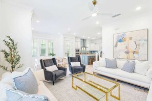 A modern living room with a sofa, two armchairs, a coffee table, and a ceiling fan.
