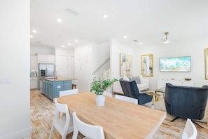 A modern kitchen with white cabinets, a wooden dining table, and a potted plant.