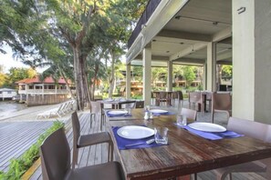 An outdoor dining area with tables and chairs, surrounded by trees and a covered walkway. - Samed Hideaway Resort (Koh Samet)