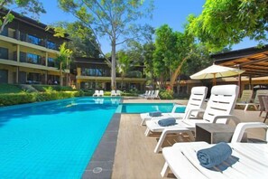 A hotel pool area with lounge chairs and umbrellas, surrounded by greenery and buildings. - Samed Hideaway Resort (Koh Samet)