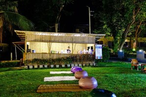 An outdoor bar area with a bamboo structure, seating arrangements, and a person behind the bar. - Samed Hideaway Resort (Koh Samet)