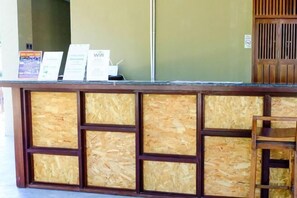 A reception desk with a wooden panel design, a wooden chair, and informational signs. - Samed Hideaway Resort (Koh Samet)