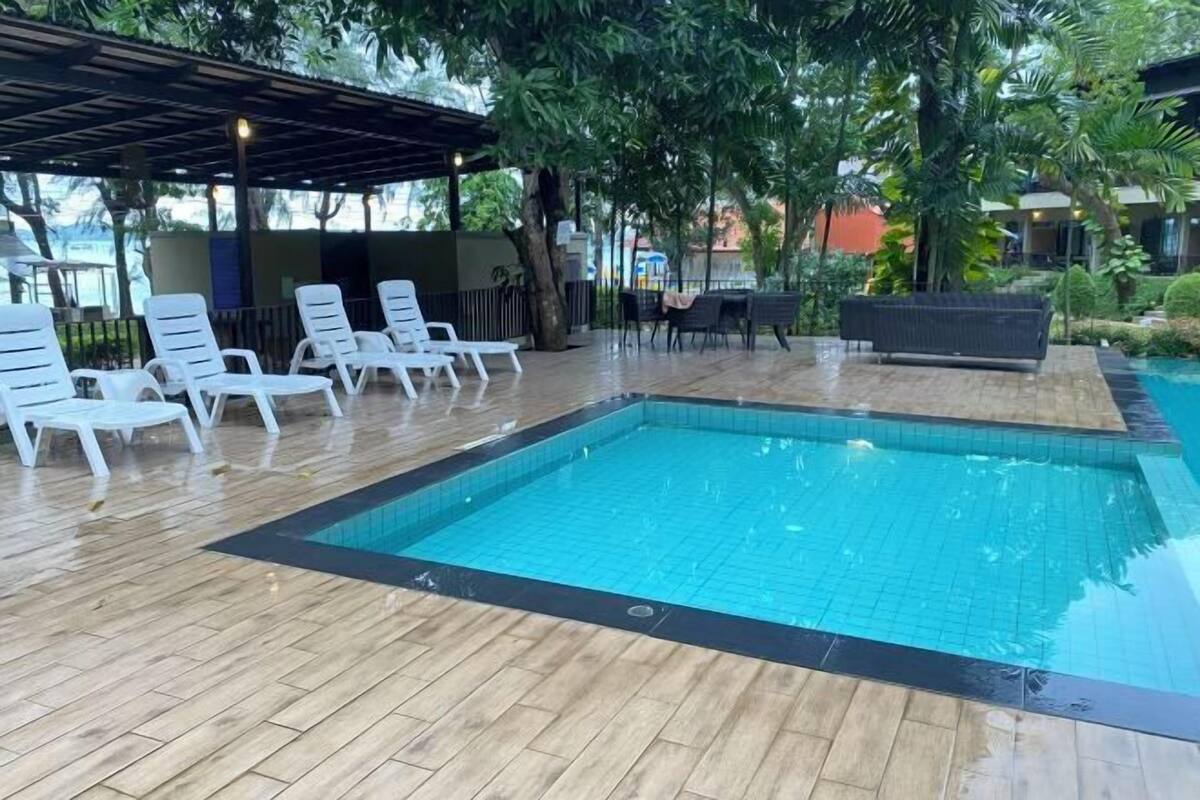 Una piscina con sillas de descanso blancas y un área de estar cubierta.