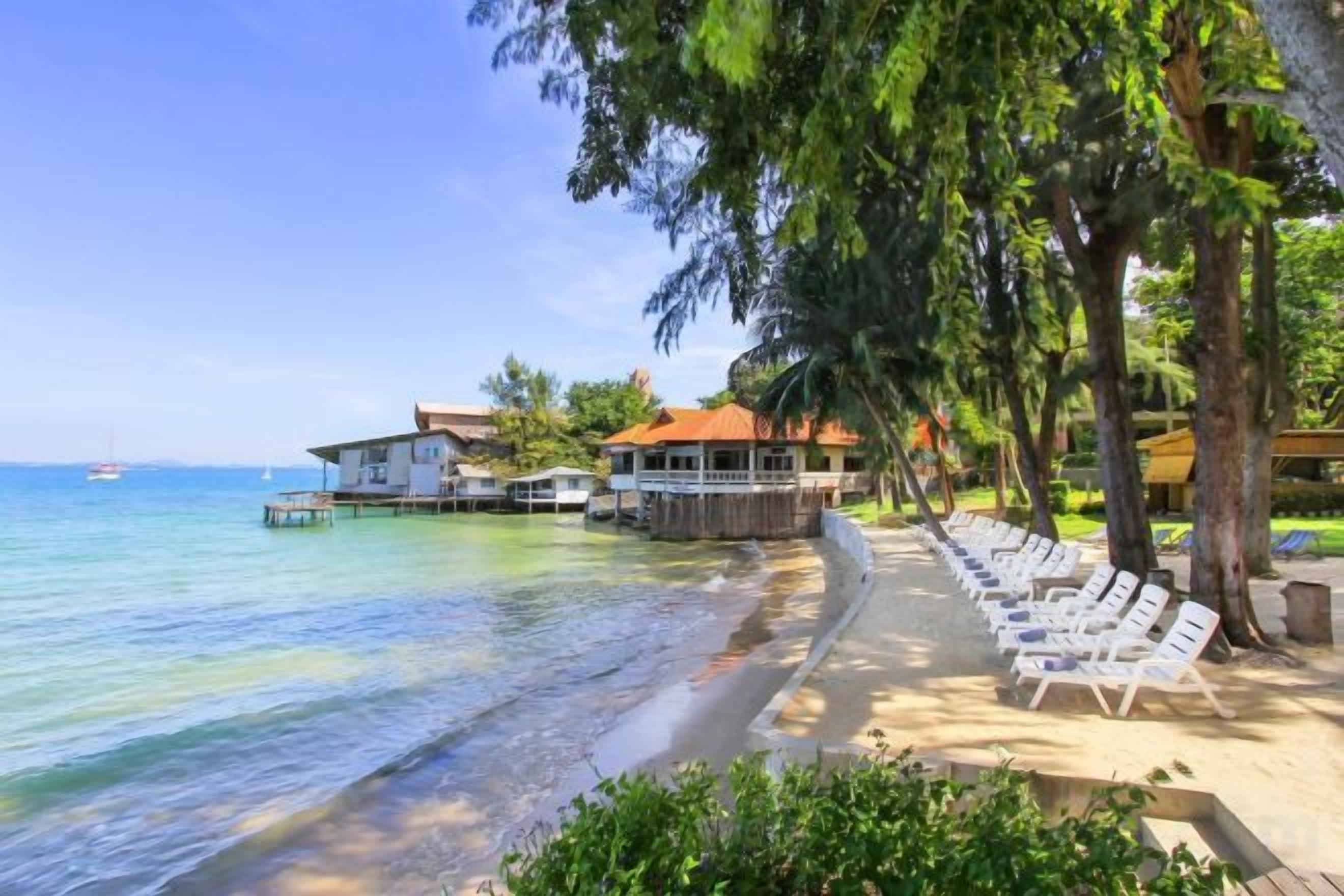 A beach with a row of sun loungers, a wooden deck, and a building with a red roof.