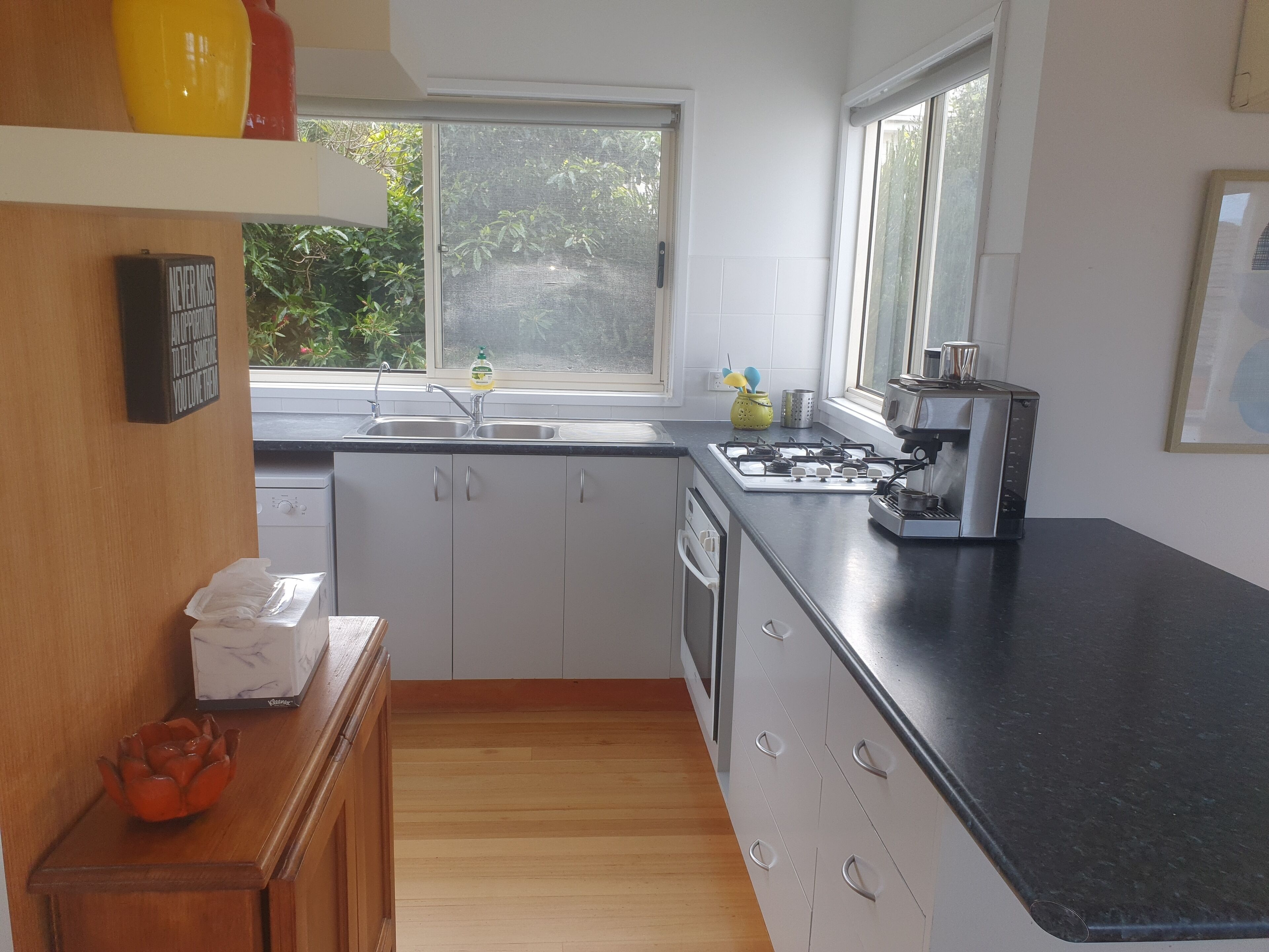 A modern kitchen with white cabinets, a black countertop, a gas stove, and a window providing natural light.