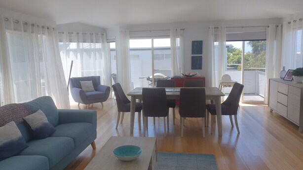 A spacious living area with a sofa, coffee table, and dining table. - 11A Seaview. 
Ocean and Otway Ranges views. Close to beach. Pet friendly. (Apollo Bay)