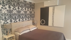 A bedroom with a bed, nightstand, lamp, and a wall-mounted artwork. - 11A Seaview. 
Ocean and Otway Ranges views. Close to beach. Pet friendly. (Apollo Bay)